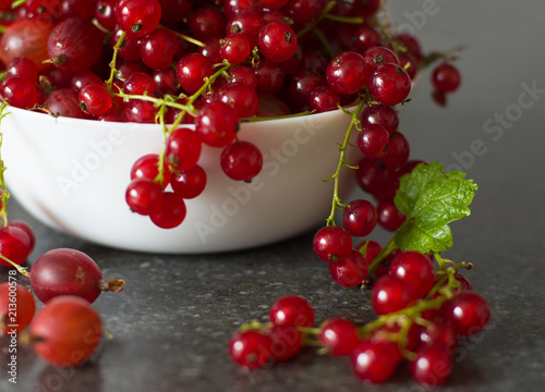 Red currant and gooseberries in a white bowl on a gray table close-up of soft focus. useful berries.