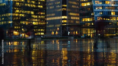 Time lapse of crowd of people walking near modern buildings in Paris business district La Defense. Night city lights, illuminated windows of office center. Concept of big city, business, job, economy