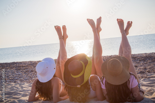 Rear view of teenage girls with hats chilling out on sandy beach in Greece / Bokeh effect / Lens flare