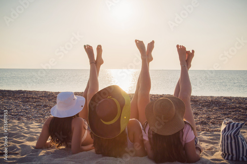 Rear view of teenage girls with hats chilling out on sandy beach in Greece / Bokeh effect / Lens flare