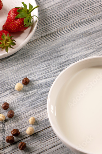 Ripe strawberries, cereal balls and a plate of milk on a gray wooden table. Top view