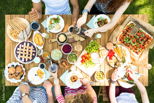 Top view of a wooden table with pizza, cherry pie, fruit, vegetables and pancakes during a vegetarian outdoor party