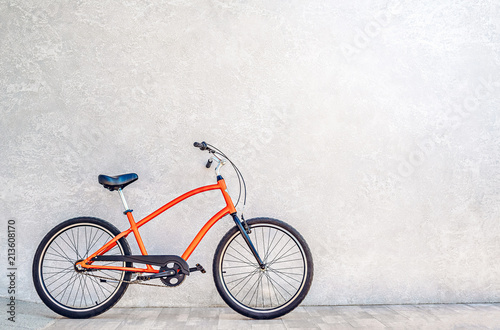 Orange color city bike against the wall with shiny silvery metallic plaster. Summertime concept