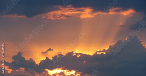 Beautiful sun rays against dark clouds at sunset, black dramatic clouds at golden sunset