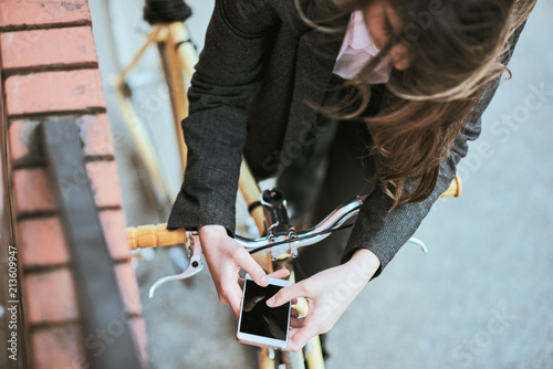 Close up of woman`s hands holding smart phone. Selective focus on phone. Woman standing against the yellow bicycle.