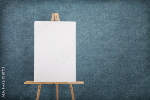 Fotografiet Wooden easel with blank canvas against a blue wall