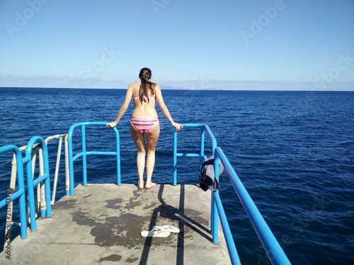woman jumping from pier to blue ocean