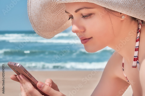 Beautiful woman in hat using her mobile phone on beach