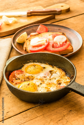 Fried eggs with tomatoes in a cast-iron frying pan on an old wooden table