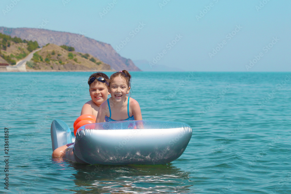 children swim in the ocean on an inflatable mattress