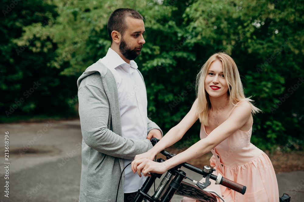 Close up of loving gentle couple riding on bike. People in love in park on sunset clodly time. Pretty girl with long hair and boy with bike. Time to kiss. Couple having a bicycles race into the nature