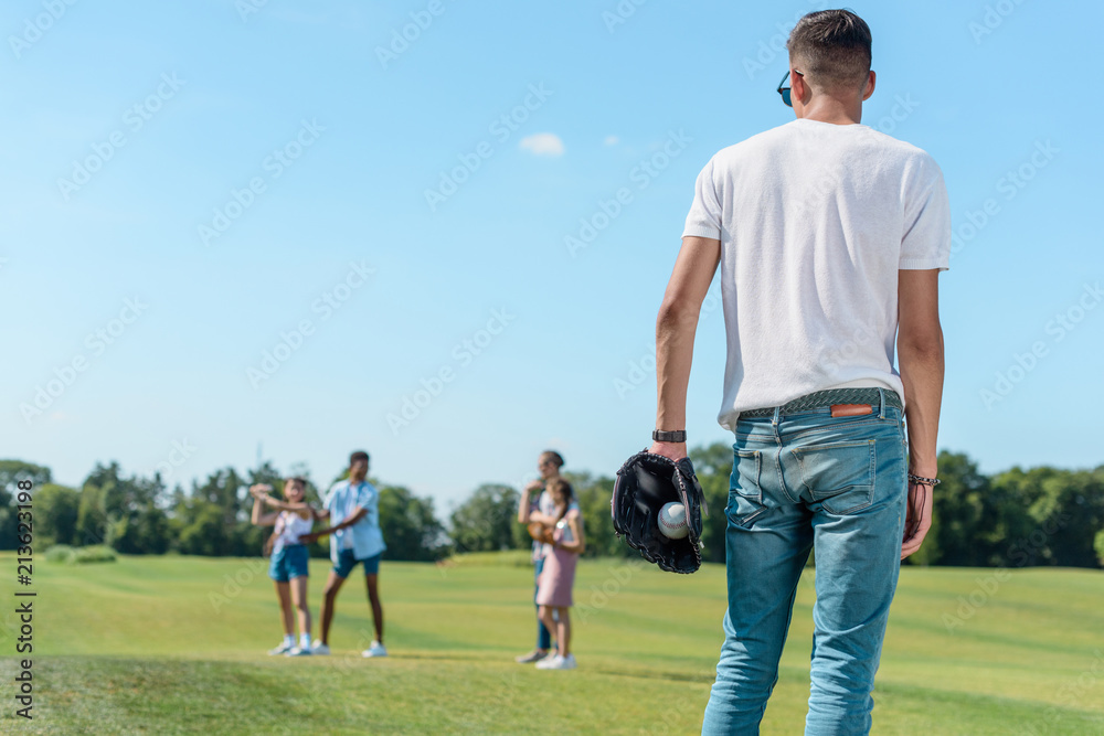 back view of teenage boy playing baseball with friends in park