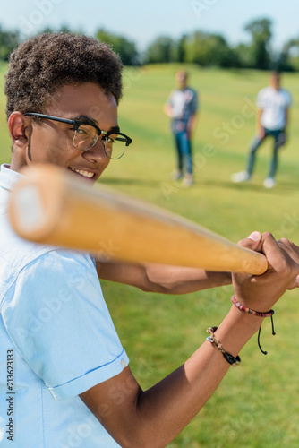 Photography selective focus of smiling african american teenager playing baseball with frien