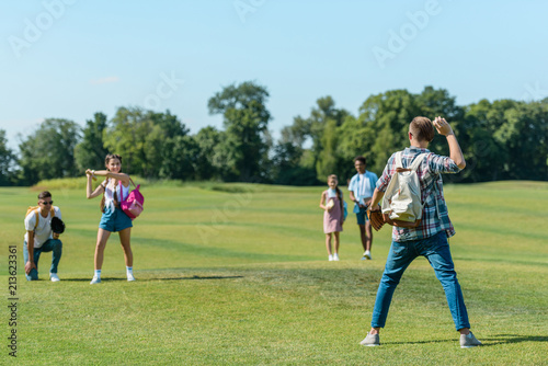 happy teenage friends playing baseball on green meadow in park