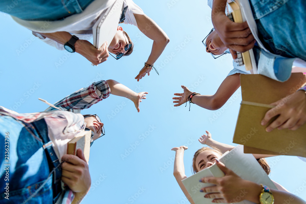 Obraz premium bottom view of happy multiethnic teenage classmates giving high five in park