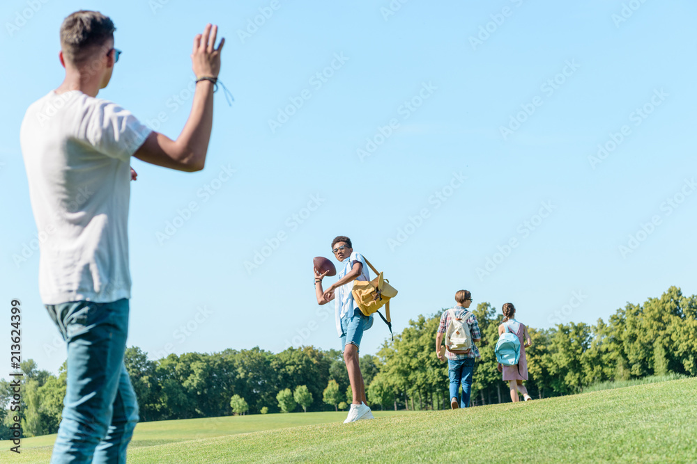 low angle view of teenagers playing with rugby ball in park low angle view of teenagers playing with rugby ball in park