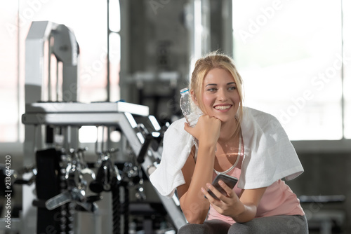 Caucasian young women are smile happy with a Smartphone and drinking water after work out exercising in gym. Technology and Living healthy lifestyle concept. © xreflex
