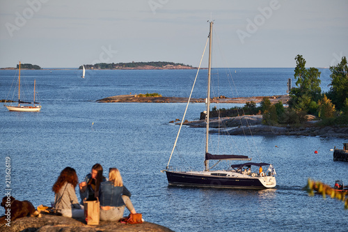 Obraz na płótnie People resting on the sea shore. Yacht, sea and islands on background. Kaivopuisto park, Helsinki, Finland w salonie