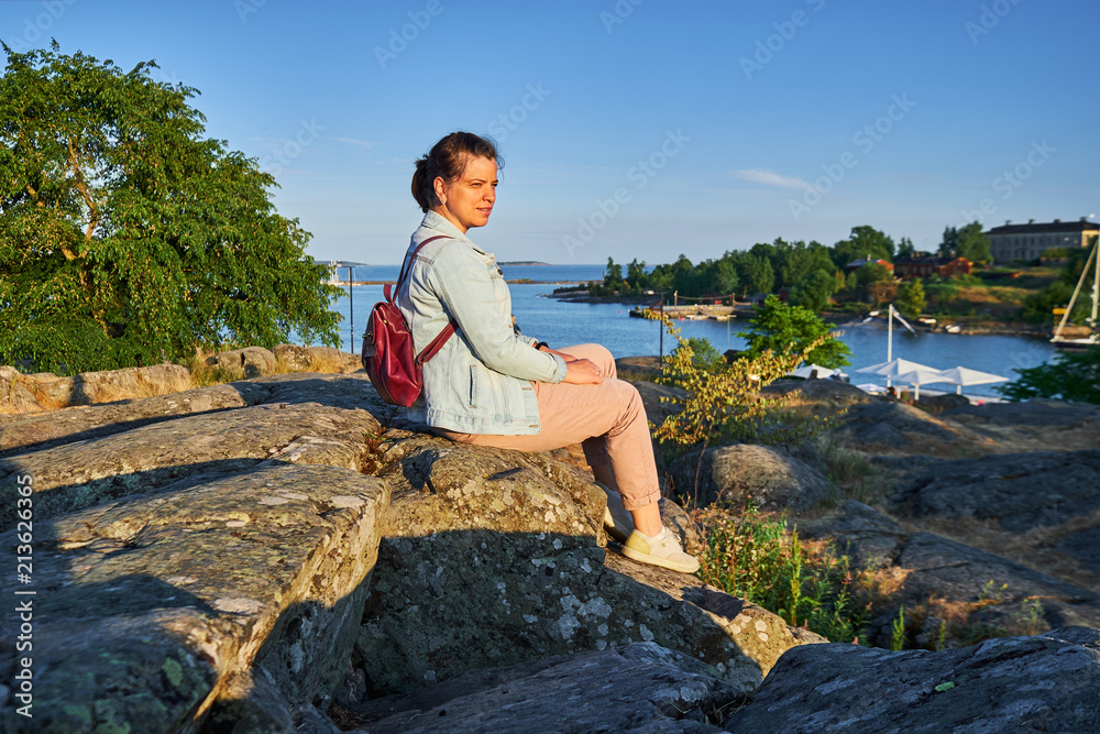 woman sitting on the stone and looking away at sunset in Kaivopuisto park, Helsinki, Finland