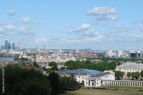 Panorama of temples and modern buildings of London from the height of the Greenwich hill against the background of a cloudy blue sky.