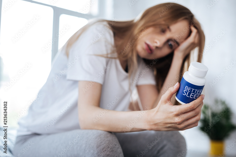Wonderful pills. Unhappy blond woman sitting and looking at her sleeping pills Wonderful pills. Unhappy blond woman sitting and looking at her sleeping pills