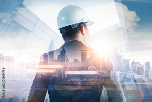 The double exposure image of the engineer standing back during sunrise overlay with cityscape image. The concept of engineering, construction, city life and future.