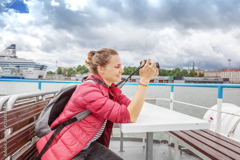 Young beautiful happy girl traveler with a camera in her hands examines the places of Helsinki, the capital of Finland with a pleasure boat. Travel to Scandinavia