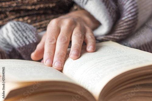 An elderly woman reads a book. The woman's hand lies on an open book. Reading the Bible and praying_