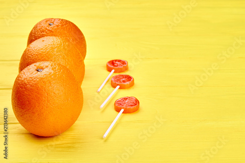 Fresh juicy oranges and sweets on wooden table. Organic oranges fruits and lollipops on yellow wooden background with text space. photo