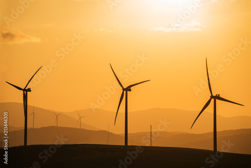 Wind power generator on a hill at sunset, silhouettes of mountain peaks. 