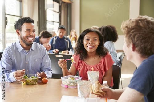 Teacher And Students Eating Lunch In High School Cafeteria During Recess photo