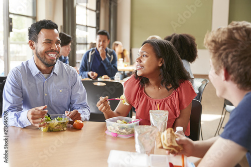 Teacher And Students Eating Lunch In High School Cafeteria During Recess