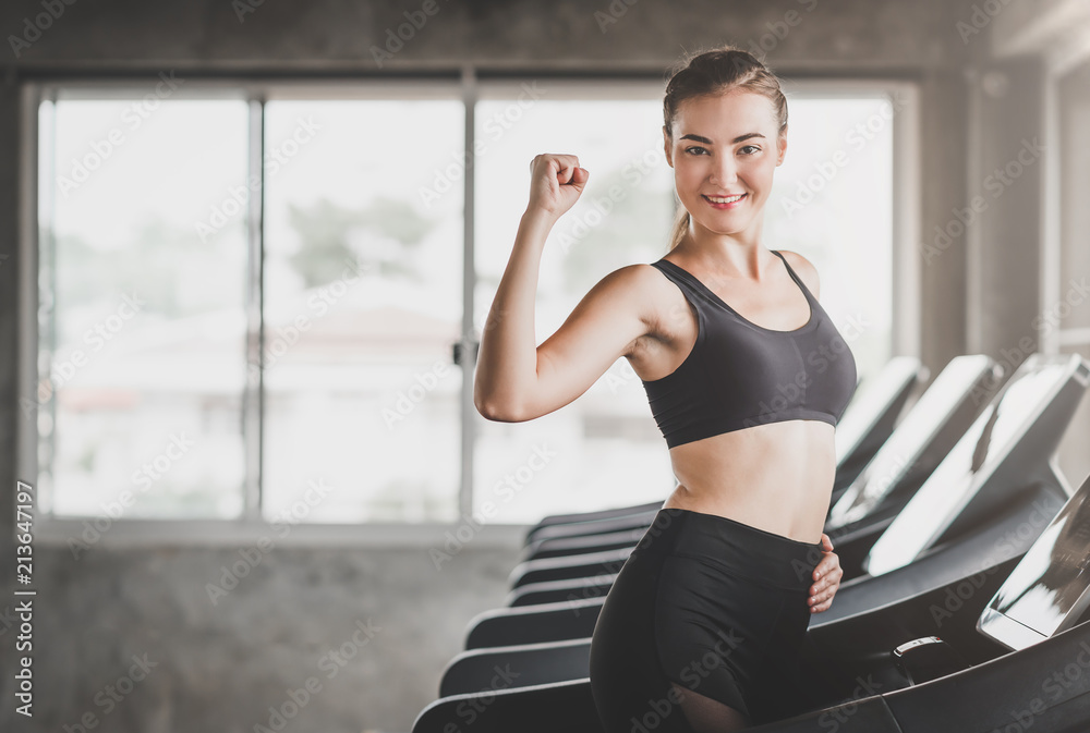 Young Caucasian woman show her bicep while using treadmill in gym