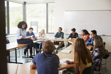 Female High School Tutor Sitting At Table With Pupils Teaching Maths Class