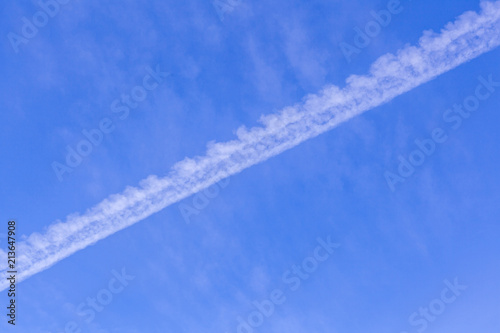 Jet trail diagonally crossing blue sky background with copy space
