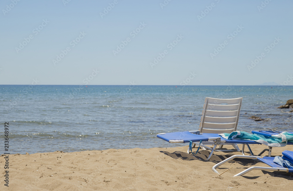 image of sun lounger and white plastic chair on the beach with sea and background