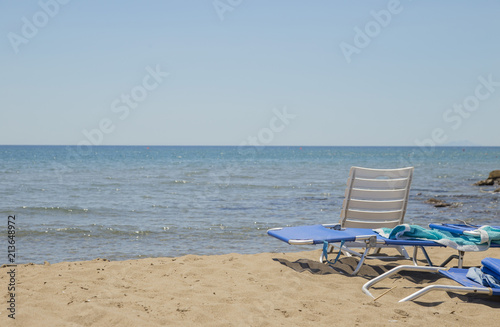 image of sun lounger and white plastic chair on the beach with sea and background © andrea