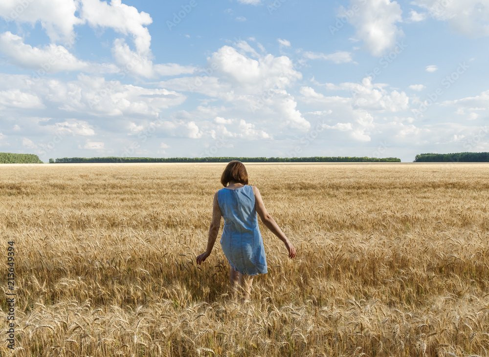 The girl is on the yellow wheat field. White clouds and blue sky in the background. The girl is on the yellow wheat field. White clouds and blue sky in the background.