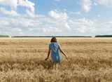 The girl is on the yellow wheat field. White clouds and blue sky in the background.