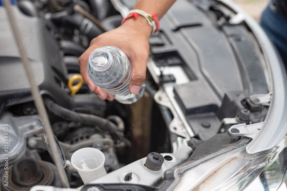 Hand pouring water for radiator in car engine. Self checking radiator water for windscreen Hand pouring water for radiator in car engine. Self checking radiator water for windscreen