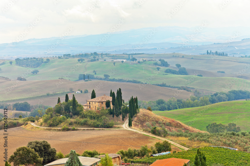 Italy. Val d'Orcia. Pienza.  Beautiful Tuscan rural landscape with autumn fields in the hills and a farmhouse with cypress and olive trees in a foggy morning