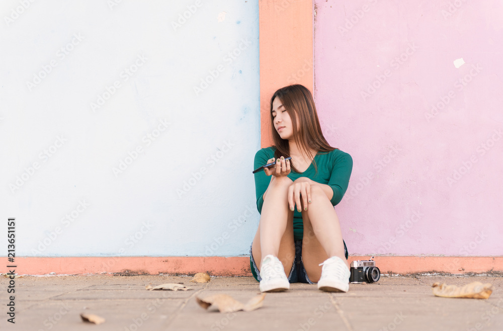 Portrait of young woman in green dress sitting sleep along a street public holding mobile phone.