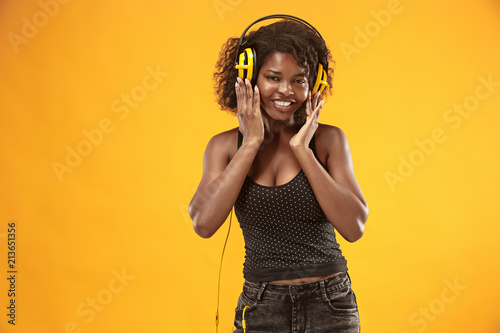 Studio portrait of adorable curly girl happy smiling during photoshoot. Stunning african woman with light-brown skin relaxing in headphones