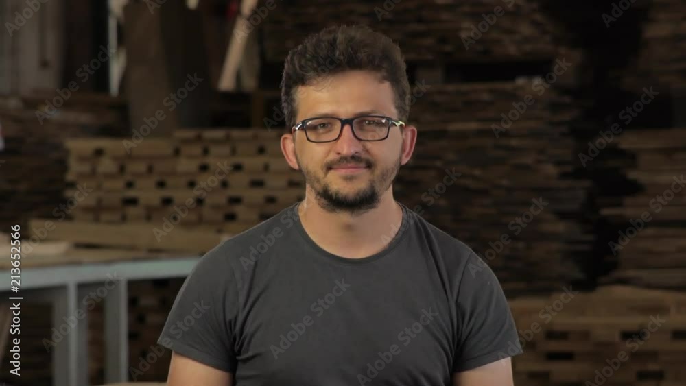 a young guy looks at the camera and smiles. glasses and a beard and a t-shirt. Against the sawmill. a young guy looks at the camera and smiles. glasses and a beard and a t-shirt. Against the sawmill.
