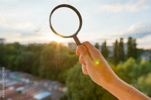 Magnifier in hand, background evening sunset, city silhouette.