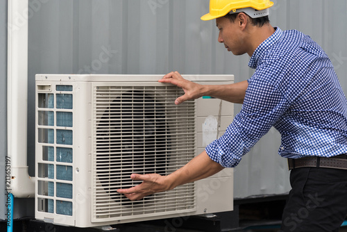 Portrait of technician in hardhat connecting outdoor air conditioning unit.
