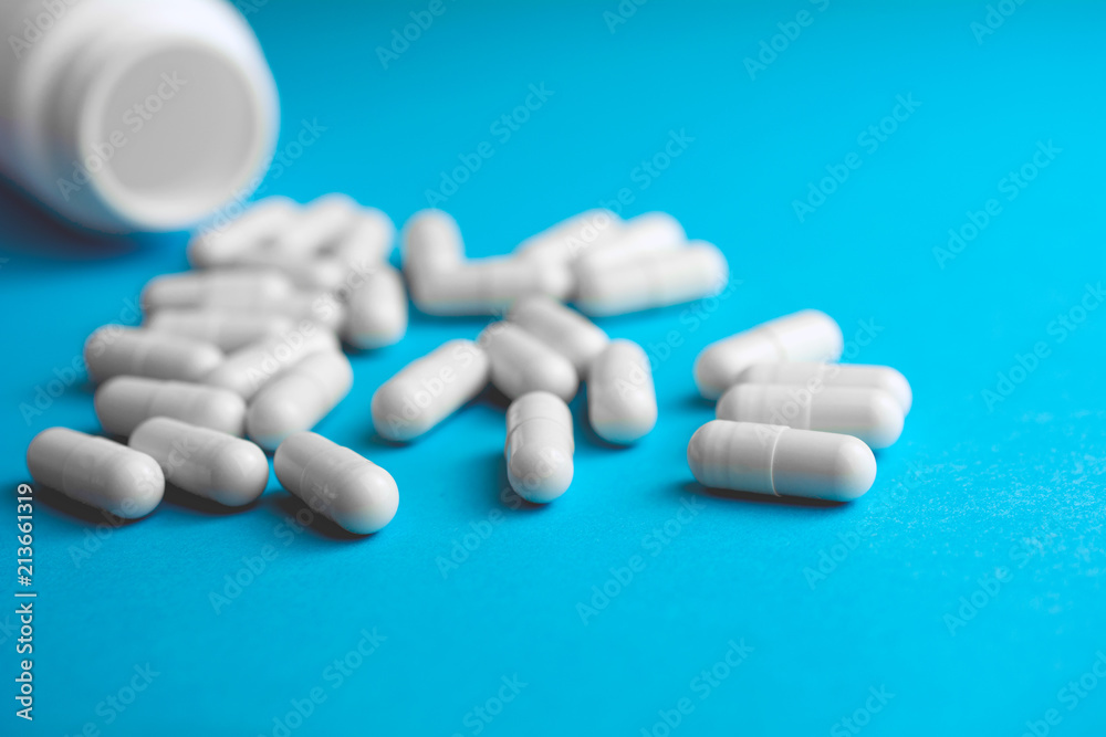 Heap of pills or tablets capsule plastic drugs bottle blue background. Pharmacy drugstore concept.