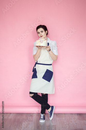 confectioner in a white apron on a pink background with a cake photo