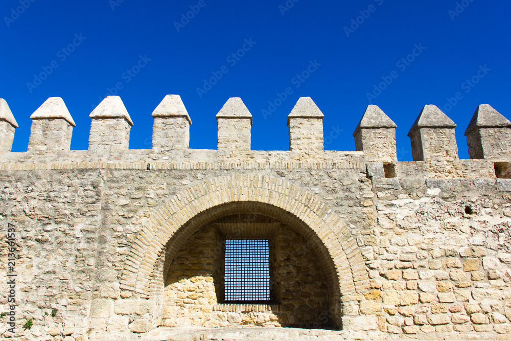Front wall of castle tower with window inside arc structure and intense blue sky on the background in Vejer white town, Andalusia. Protection, security, defense concepts