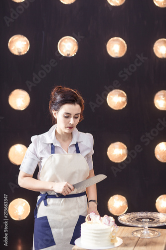 confectioner in a white apron on a pink background with a cake photo